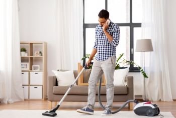 household and cleaning concept - indian man with vacuum cleaner calling on smartphone at home. man with vacuum cleaner calling on cell at home