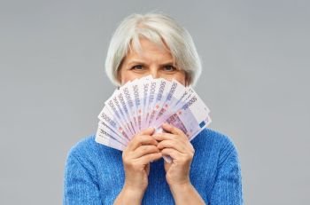 savings, finances and people concept - smiling senior woman hiding face behind fan of five hundred euro money banknotes. senior woman with hundreds of euro money banknotes