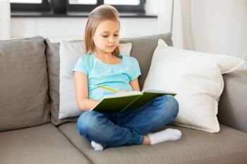 people, childhood and bedtime concept - little girl with diary and pencil sitting on sofa at home. little girl with diary sitting on sofa at home