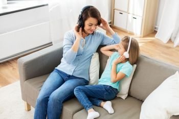 people, family and technology concept - happy mother and daughter in headphones listening to music at home. mother and daughter in headphones listen to music