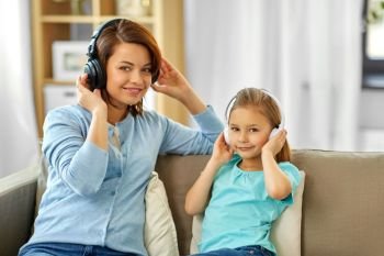 people, family and technology concept - happy mother and daughter in headphones listening to music at home. mother and daughter in headphones listen to music