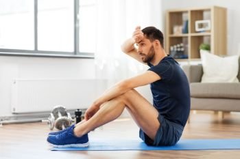 sport, fitness and healthy lifestyle concept - tired man sitting on exercise mat at home. tired man sitting on exercise mat at home