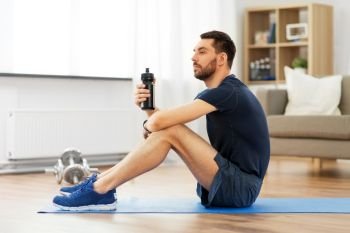 sport, fitness and healthy lifestyle concept - man drinking water from bottle during training at home. man drinking water during training at home