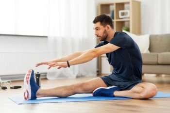 sport, fitness and healthy lifestyle concept - man stretching leg on exercise mat at home. man stretching leg on exercise mat at home