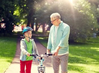 family, generation, safety and people concept - happy grandfather and boy with bicycle and bike helmet talking at summer park. grandfather and boy with bicycle at summer park