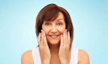 beauty, skin care and old people concept - portrait of smiling senior woman touching her face over blue background. portrait of smiling senior woman touching her face