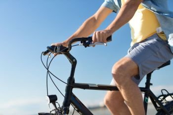 people, leisure and lifestyle concept - close up of young man riding bicycle along summer beach. close up of man riding bicycle along summer beach
