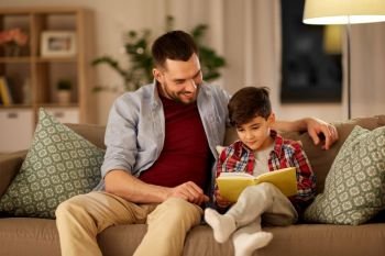 family, childhood, fatherhood, leisure and people concept - happy smiling father and little son reading book on sofa at home. happy father and son reading book sofa at home