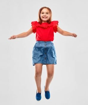 childhood, fun and motion concept - happy smiling girl in red shirt and skirt jumping over grey background. happy smiling girl in red shirt and skirt jumping