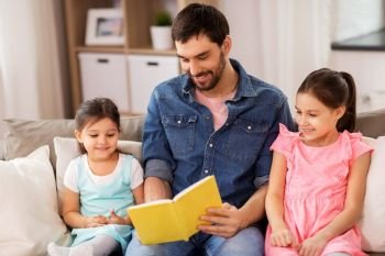 family, leisure and people concept - happy father with daughters reading book at home. happy father with daughters reading book at home