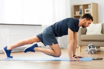sport, fitness and healthy lifestyle concept - man with tablet computer doing running plank exercise at home. man doing running plank exercise at home