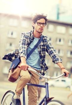 people, style, leisure and lifestyle - young hipster man with shoulder bag and earphones riding fixed gear bike on city street. young hipster man with bag riding fixed gear bike