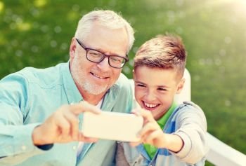 family, generation, technology and people concept - happy grandfather and grandson with smartphone taking selfie at summer park. old man and boy taking selfie by smartphone