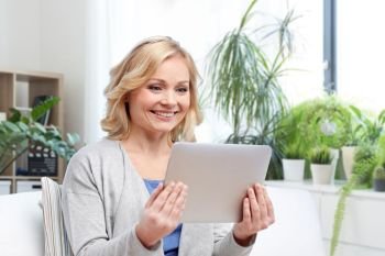 people, technology and internet concept - happy middle aged woman with tablet pc computer at home. middle aged woman with tablet computer at home