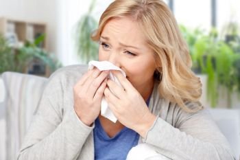 cold, allergy and health problem concept - ill woman or allergic blowing nose to tissue at home. ill woman blowing nose to tissue at home