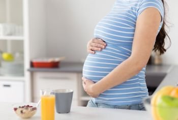 pregnancy, healthy eating and maternity concept - close up of pregnant woman touching her belly with breakfast on kitchen table at home. close up of pregnant woman touching her belly