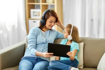 people, family and technology concept - happy mother and daughter with tablet pc computer and headphones listening to music at home. mother and daughter listen to music on tablet pc