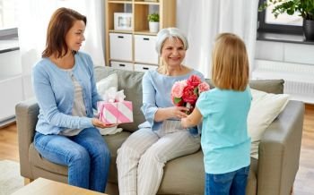family, generation and birthday - happy mother with gift box and daughter giving flowers to grandmother at home. granddaughter giving flowers to grandmother