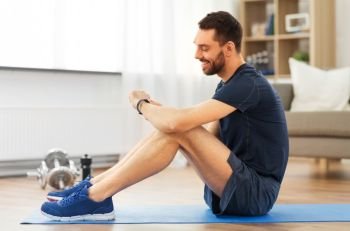 sport, technology and healthy lifestyle concept - smiling man with fitness tracker exercising at home. smiling man with fitness tracker exercising at home