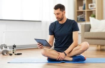 sport, fitness and healthy lifestyle concept - man with tablet computer sitting on exercise mat at home. man with tablet computer on exercise mat at home