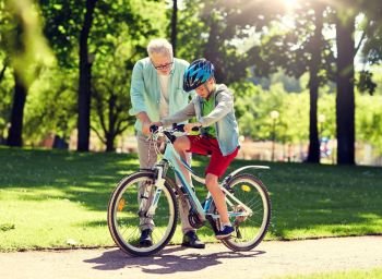family, generation, safety and people concept - happy grandfather teaching boy how to ride bicycle at summer park. grandfather and boy with bicycle at summer park