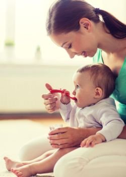 family, food, child, eating and parenthood concept - happy smiling mother with puree and spoon feeding little baby at home. happy mother with spoon feeding baby at home