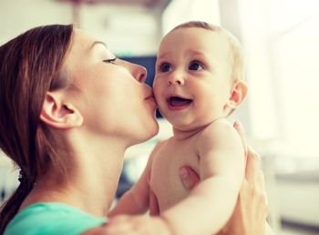 family, child and parenthood concept - close up of happy smiling young mother kissing little baby at home. happy young mother kissing little baby at home