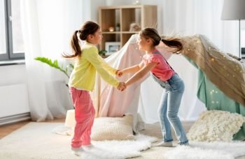 childhood, hygge and friendship concept - happy girls playing near kids tent or teepee at home. happy girls playing near kids tent at home
