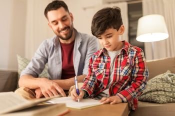 education, family and homework concept - happy father and son with book writing to notebook at home. father and son doing homework together