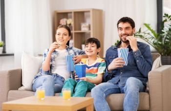 family, leisure and people concept - happy mother, father and son eating popcorn and watching tv at home. happy family with popcorn watching tv at home