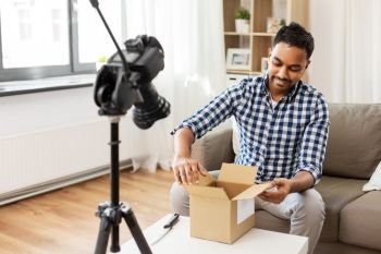mail delivery, shipment and blogging concept - happy indian male blogger opening parcel box and recording video by camera at home. male video blogger opening parcel box at home