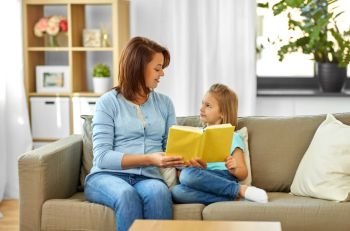 people, family and education concept - happy daughter with mother reading book at home. happy girl with mother reading book at home