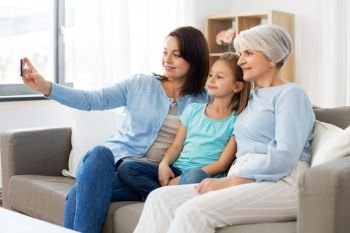 family, generation and technology concept - happy mother, daughter and grandmother taking selfie by smartphone at home. mother, daughter and grandmother taking selfie