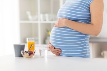pregnancy, healthy eating and maternity concept - close up of pregnant woman touching her belly with breakfast on kitchen table at home. close up of pregnant woman touching her belly
