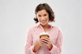 people and bedtime concept - happy young woman in pajama with takeaway paper cup of coffee over grey background. happy young woman in pajama with cup of coffee