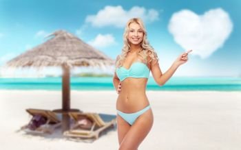 summer holidays, vacation and travel concept - happy smiling young woman in bikini swimsuit pointing finger over tropical beach of maldives background. happy smiling young woman in bikini on beach
