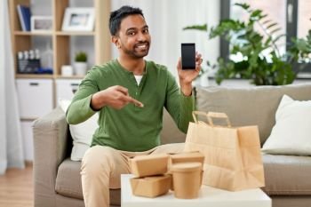 technology, consumption and people concept - smiling indian man using smartphone for food delivery at home. indian man using smartphone for food delivery