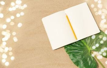 vacation, travel and summer concept - notebook with pencil and leaf on beach sand. notebook with pencil and leaf on beach sand