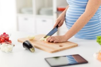 pregnancy, cooking food and healthy eating concept - close up of pregnant woman with kitchen knife chopping onion at home. close up of pregnant woman cooking food at home
