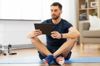 sport, fitness and healthy lifestyle concept - man with tablet computer sitting on exercise mat at home. man with tablet computer on exercise mat at home