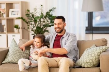 family, fatherhood and people concept - happy father and daughter with popcorn watching tv at home. happy father and daughter watching tv at home