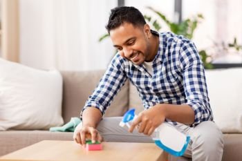 household and people concept - indian man cleaning table with detergent at home. indian man cleaning table with detergent at home