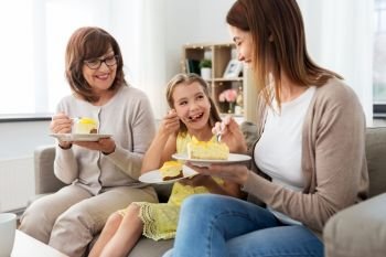 family, generation and food concept - smiling mother, daughter and grandmother eating cake at home. mother, daughter and grandmother eating cake