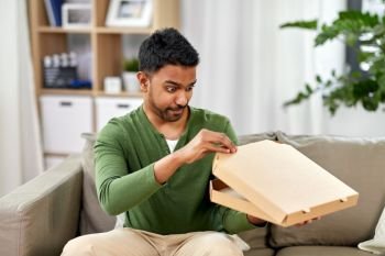 food delivery, consumption and people concept - excited indian man looking inside of takeaway pizza box at home. indian man looking inside of takeaway pizza box