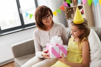 family, greetings and celebration concept - happy grandmother giving her granddaughter birthday gift at home. grandmother giving granddaughter birthday gift
