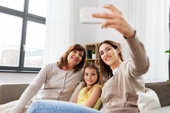 family, generation and technology concept - happy mother, daughter and grandmother taking selfie by smartphone at home. mother, daughter and grandmother taking selfie