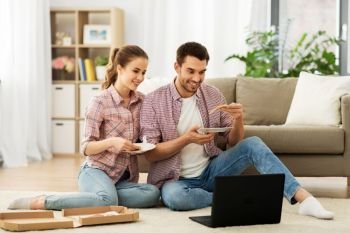 leisure, people and technology concept - happy couple with laptop computer eating takeaway pizza at home. happy couple with laptop eating pizza at home
