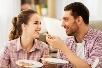 food, leisure and people concept - happy couple eating pizza at home. happy couple eating pizza at home