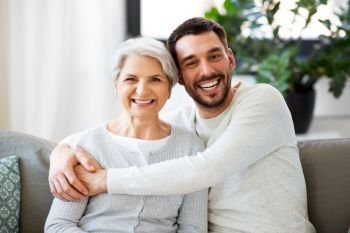 family, generation and people concept - happy smiling senior mother with adult son hugging at home. senior mother with adult son hugging at home