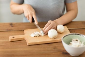 cooking, culinary and edible mushrooms concept - close up of woman chopping champignons by kitchen knife on wooden cutting board. woman cutting champignons by knife on board